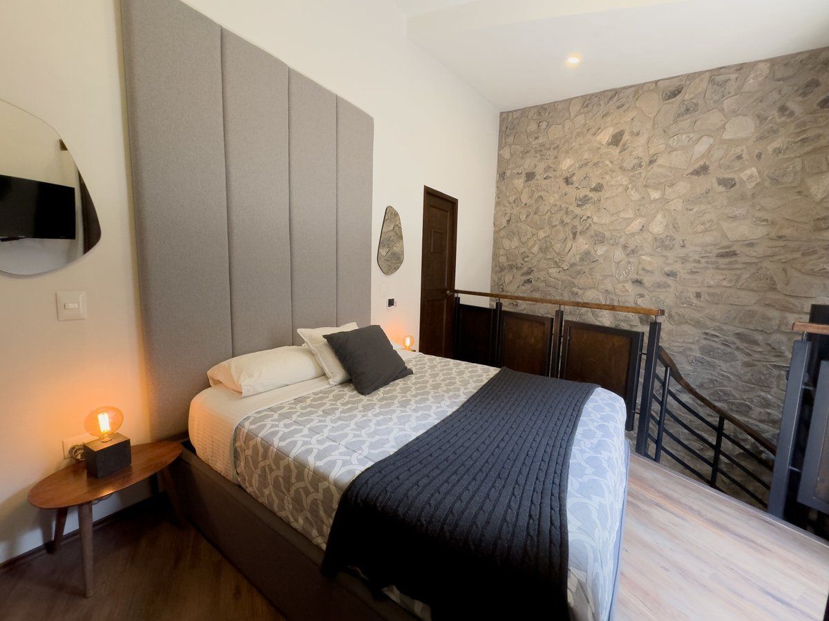 Cozy bedroom with a bed, gray upholstered headboard, wood floor, and stone accent wall
