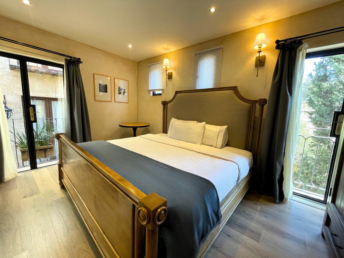 Elegant bedroom with a wooden bed, gray bedding, and large windows letting in natural light