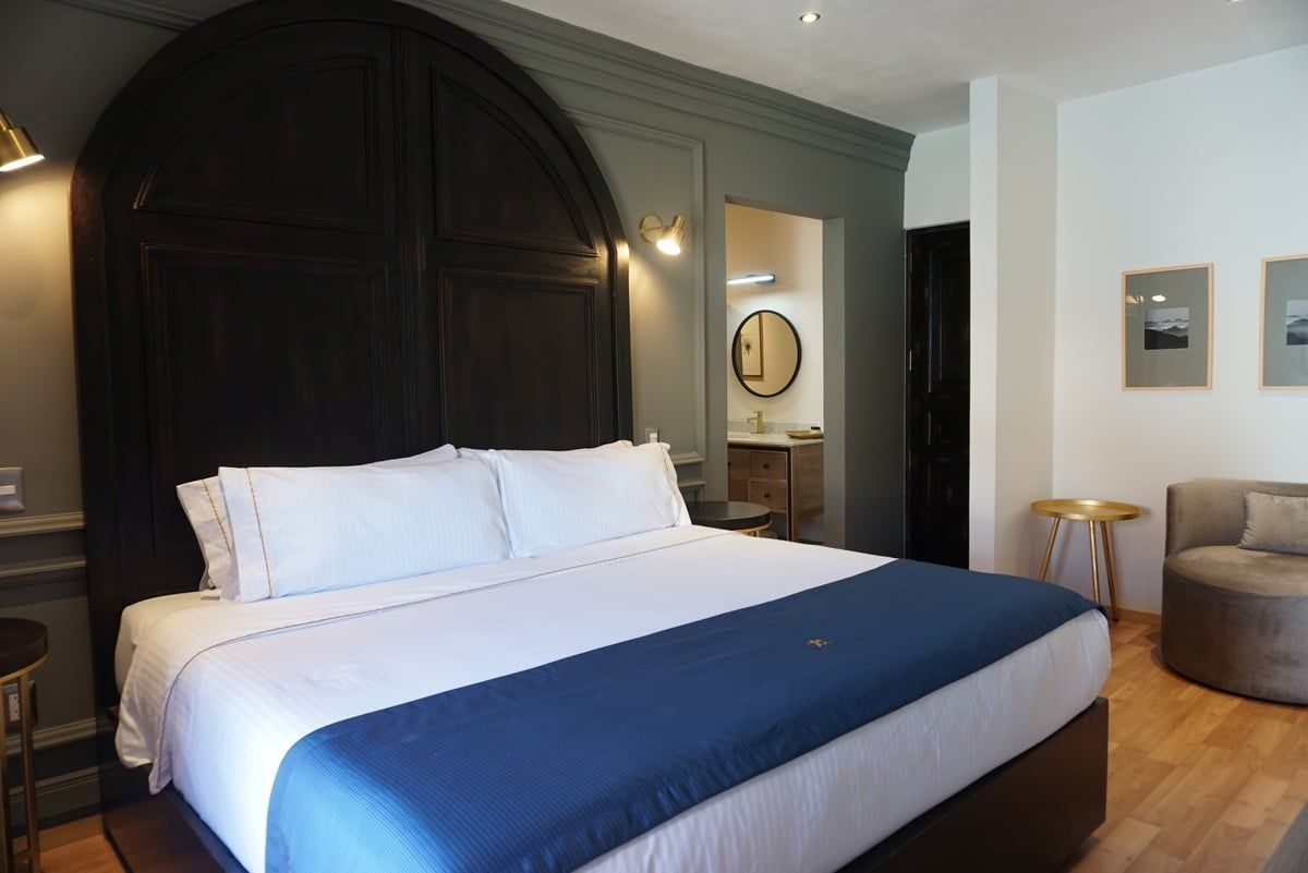 Hotel room with a large bed, dark headboard, blue runner, and seating area by the window.