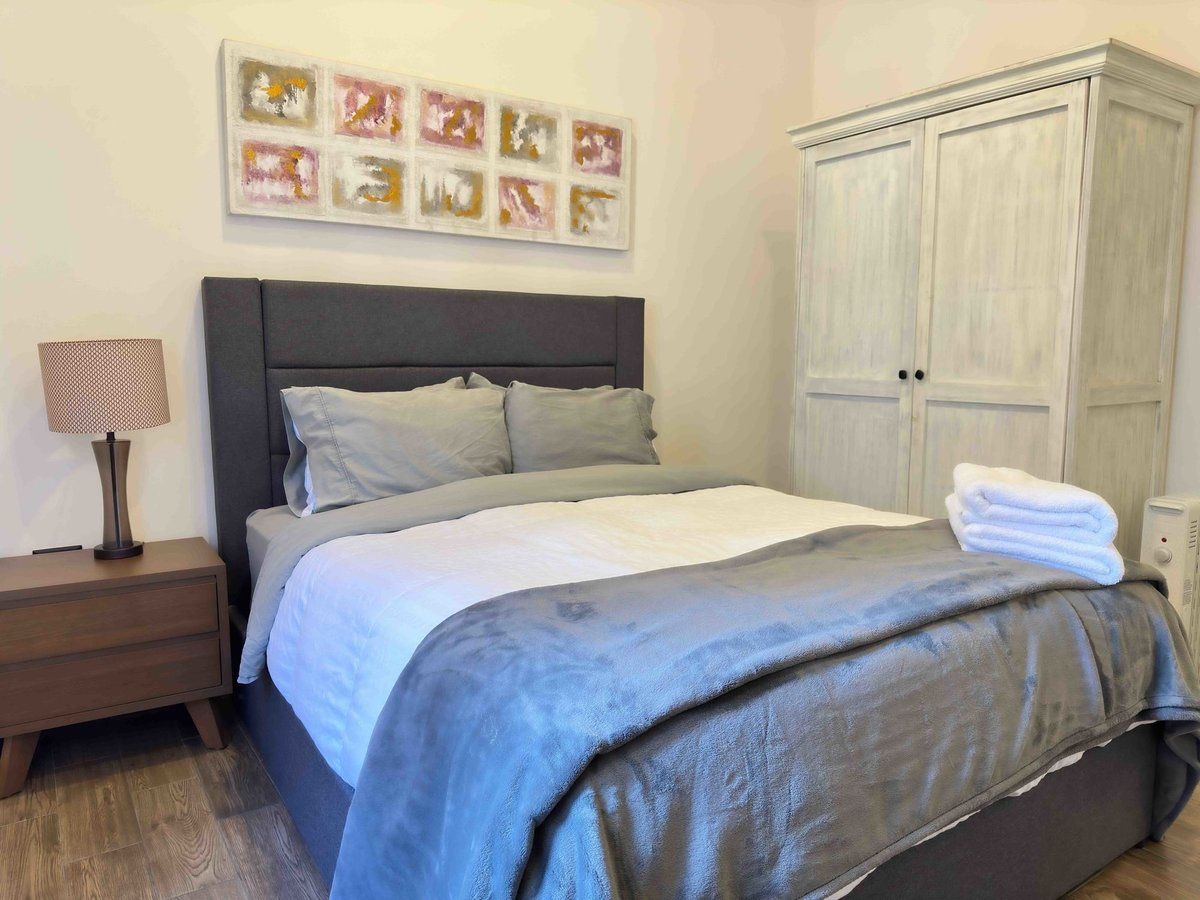 Neatly made bedroom with gray bed, bedside table, wall art, and white wardrobe.