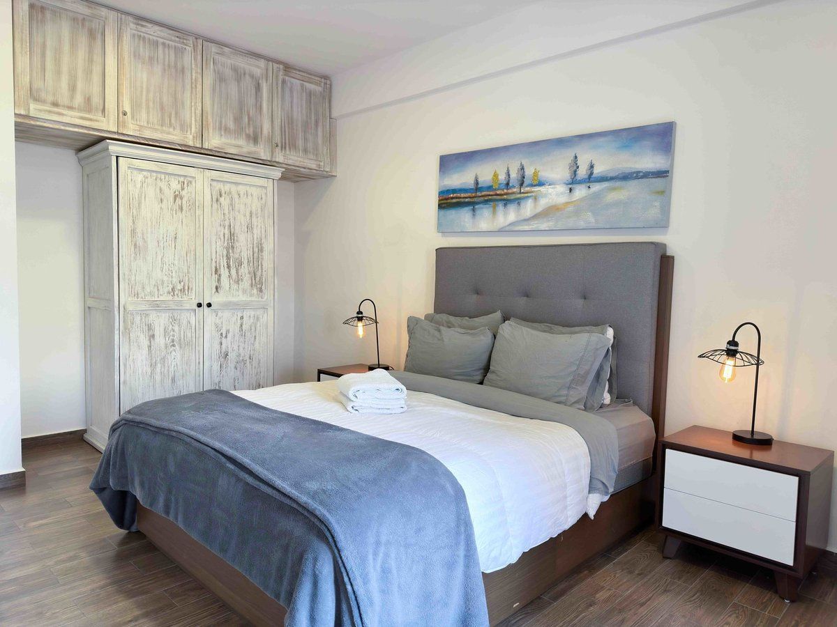 Cozy bedroom with a bed, gray headboard, bedside lamps, and a coastal painting above the bed