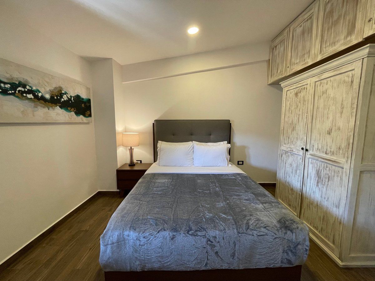 Bedroom with a gray bedspread, white headboard, and large cream wardrobe in a softly lit room