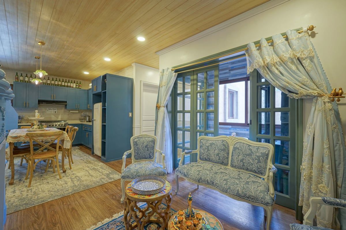 Blue-toned living room and kitchen with sofa, dining table, and open French doors.