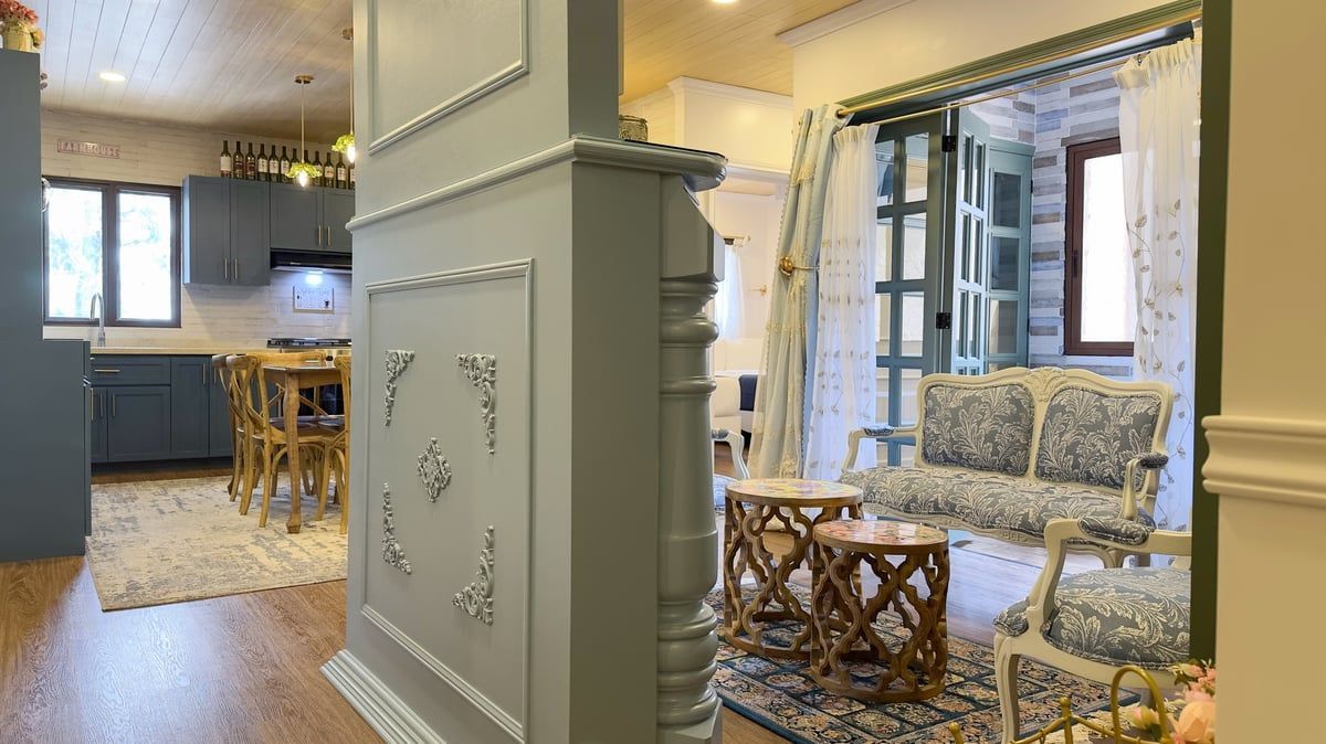 Bright living room with patterned sofas, wicker chairs, and a kitchen in the background