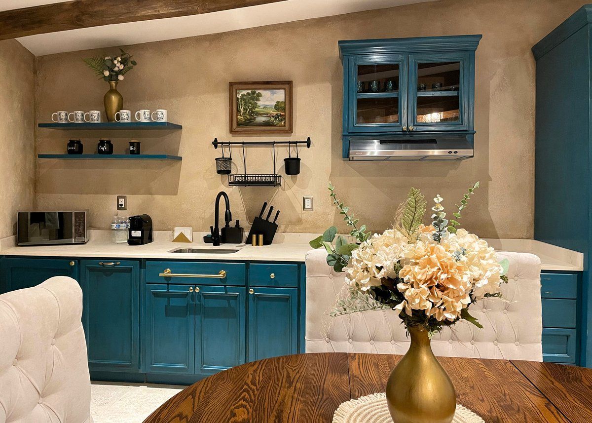 Teal kitchen with open shelves, white counters, and a vase of flowers on a round table