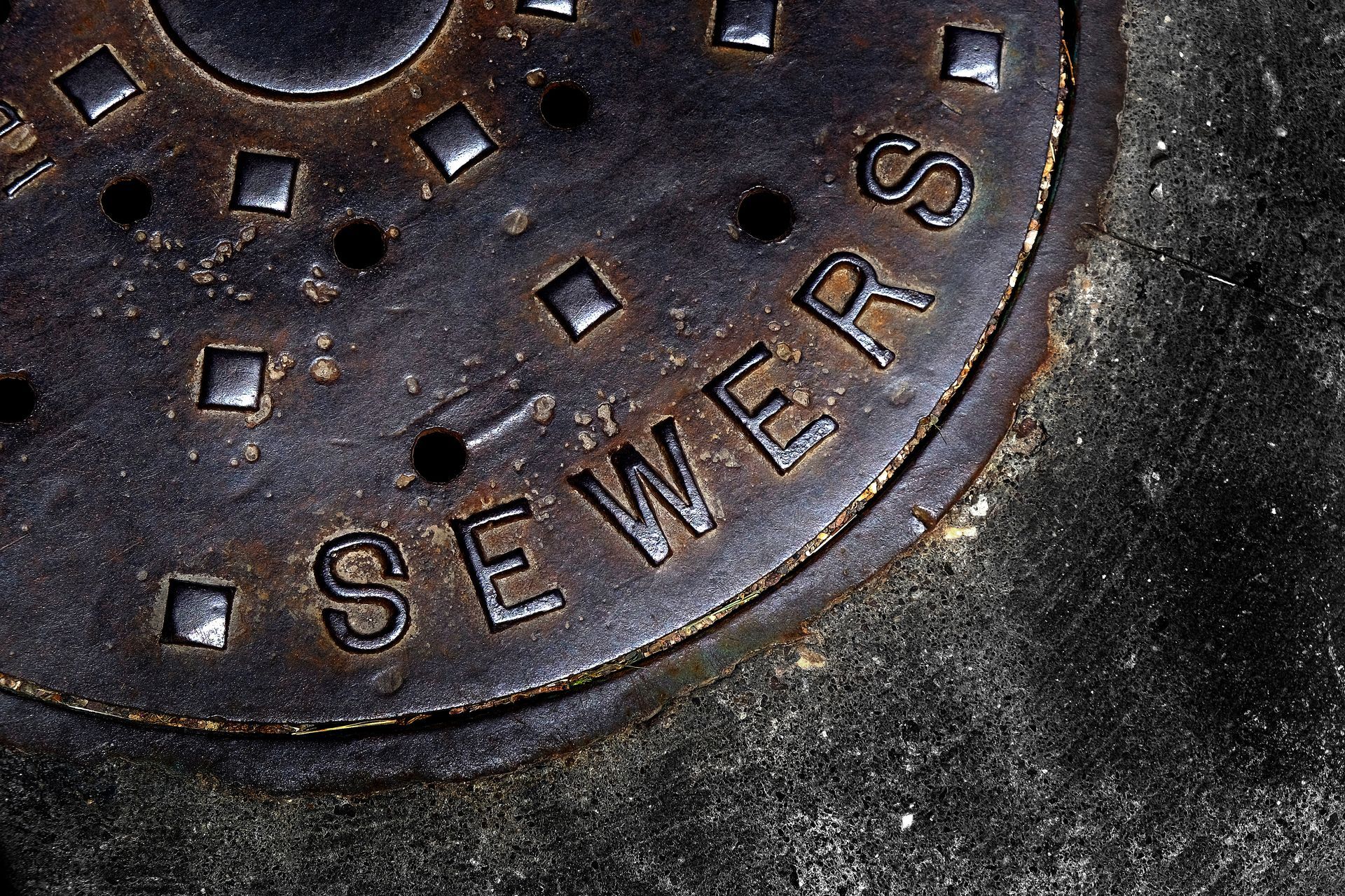 Rusty manhole cover with “SEWERS” text embedded in pavement. Rusty manhole cover with “SEWERS” text embedded in pavement.