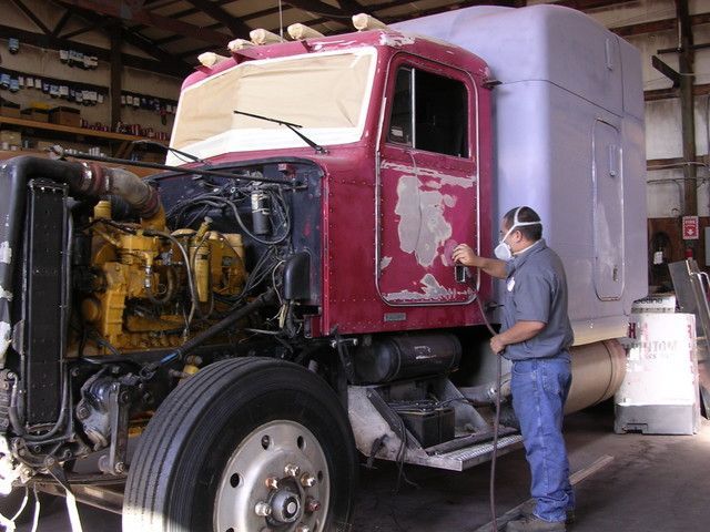 Mechanic inspecting a red semi-truck in a garage, with the hood open and engine exposed