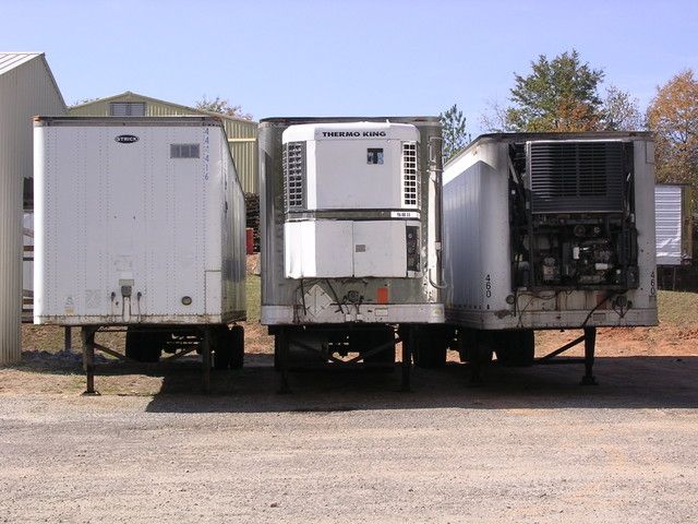 Three large white refrigerated cargo trailers parked side by side on a gravel lot.