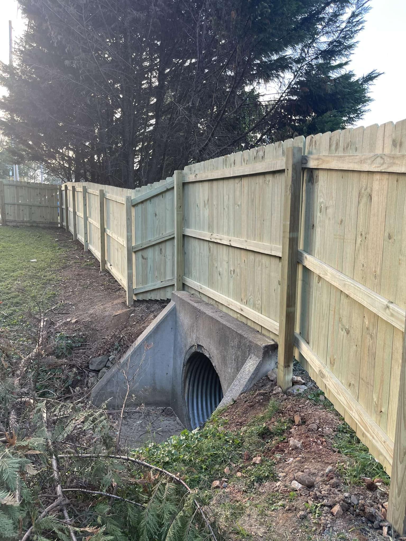 A wooden fence surrounds a concrete pipe in a yard.