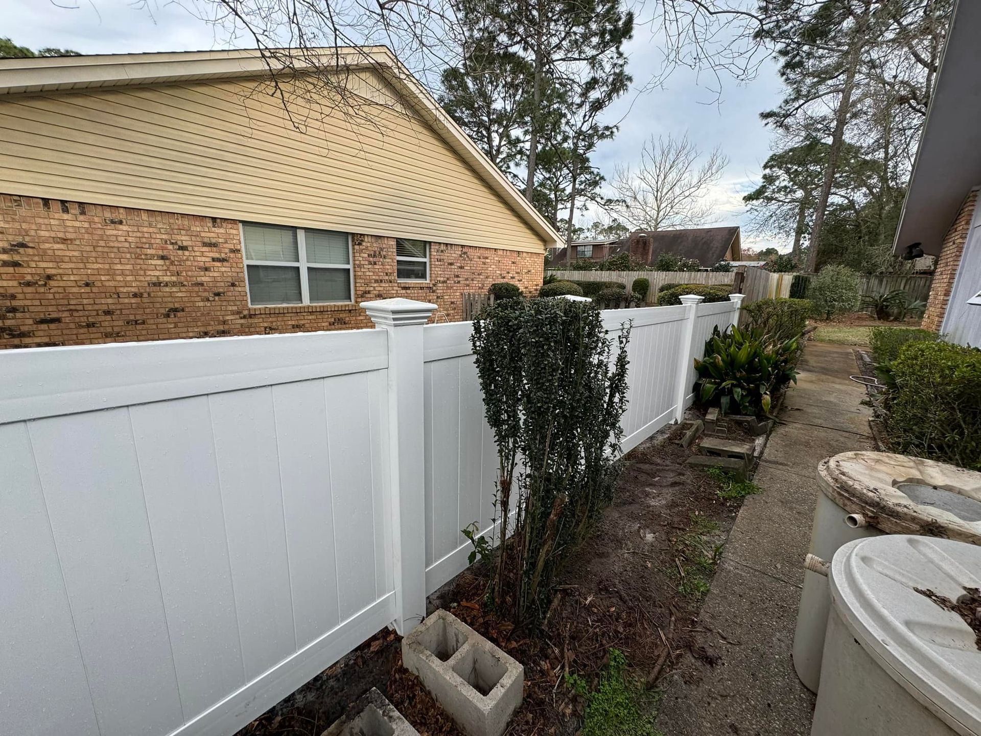 White fence bordering a yard next to a brick building. Overcast sky.
