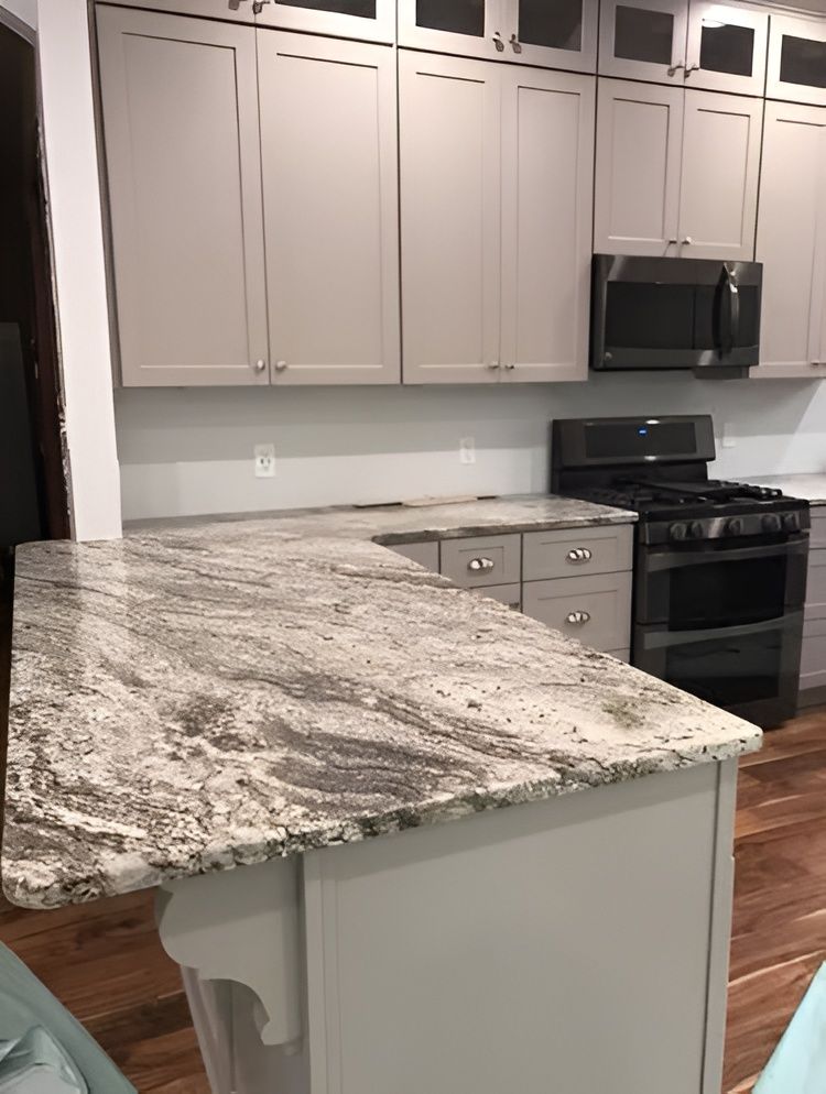 Modern kitchen with gray cabinets, granite island, and stainless steel stove and microwave.