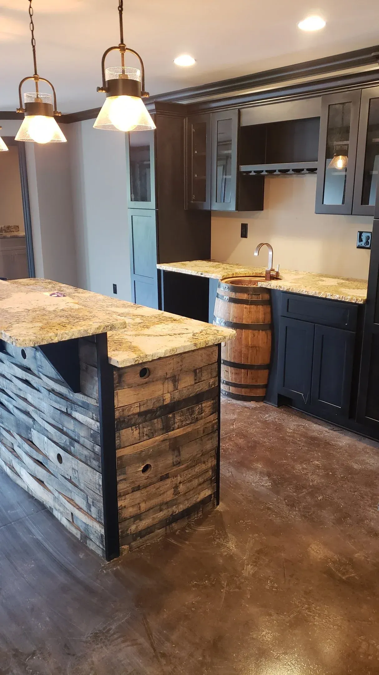 Rustic kitchen with granite island, pendant lights, dark cabinets, and wood-accented bar stools