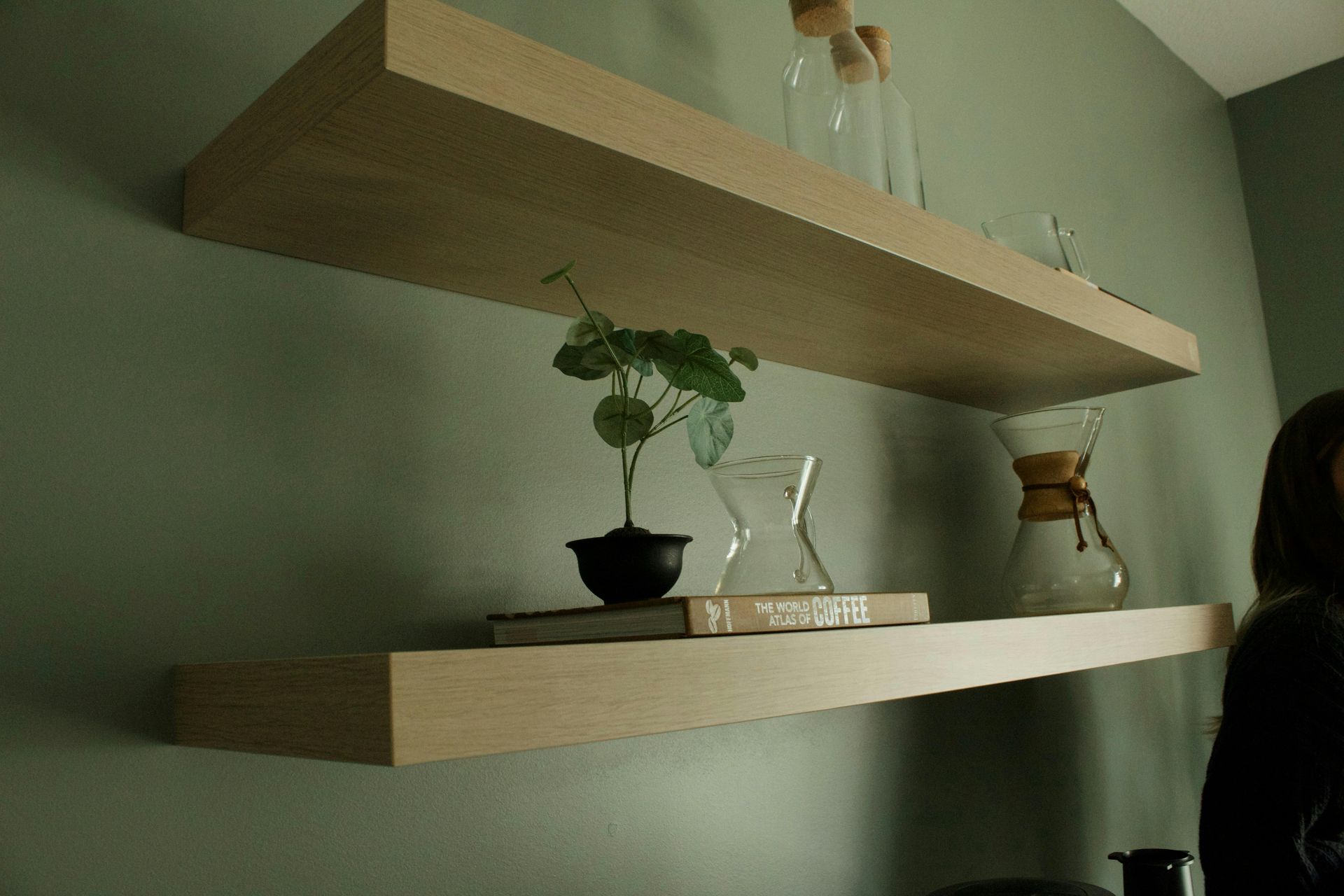 Two floating wooden shelves with a potted plant, decor, and a small chair in a muted room