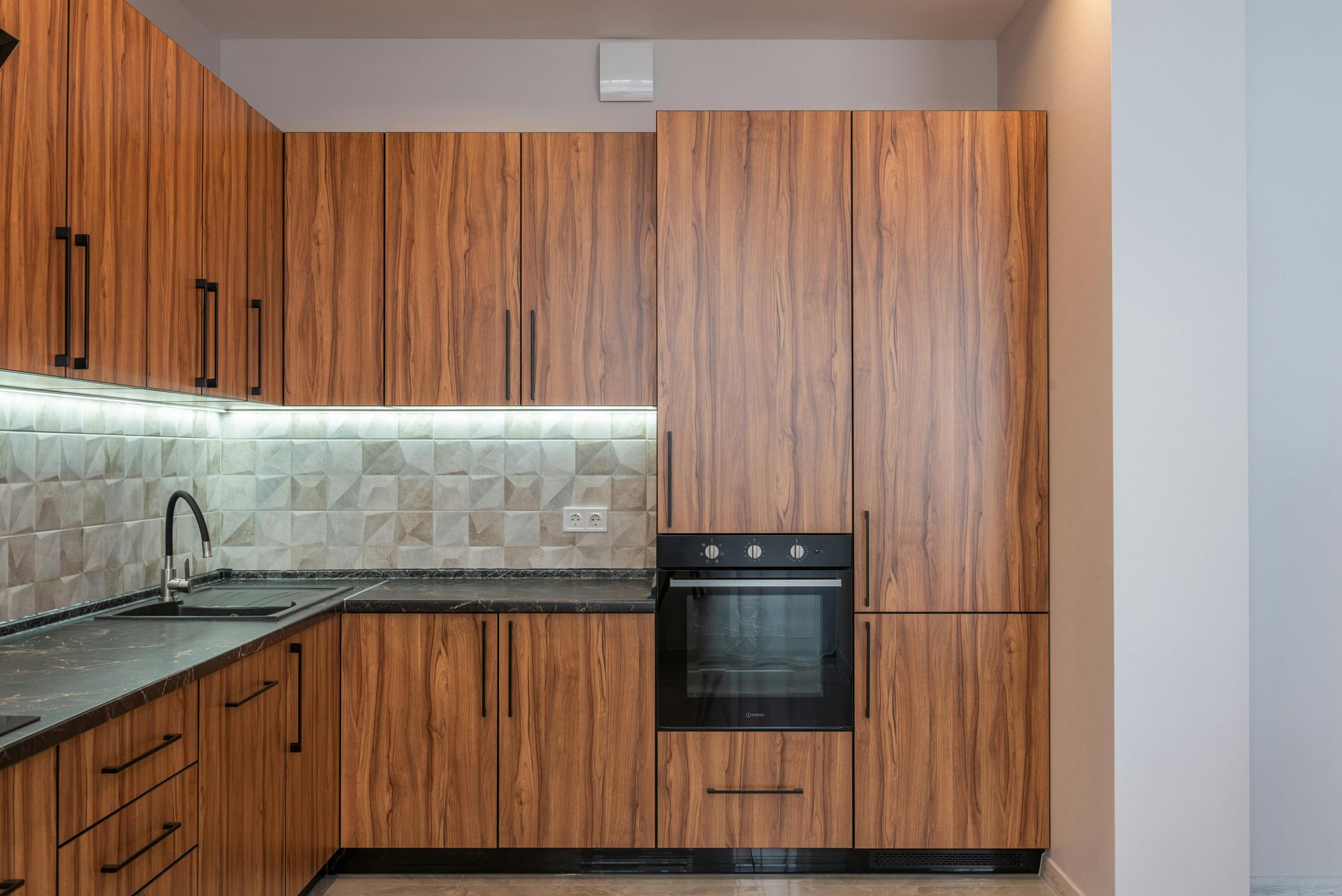 Modern kitchen with wood cabinets, black countertops, tiled backsplash, and built-in oven