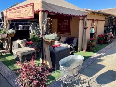Outdoor patio furniture display with tan canopy, wicker chairs, and potted plants outside a shop.