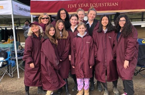 Group in maroon rain ponchos standing in front of a Five Star Equestrian booth at an outdoor event