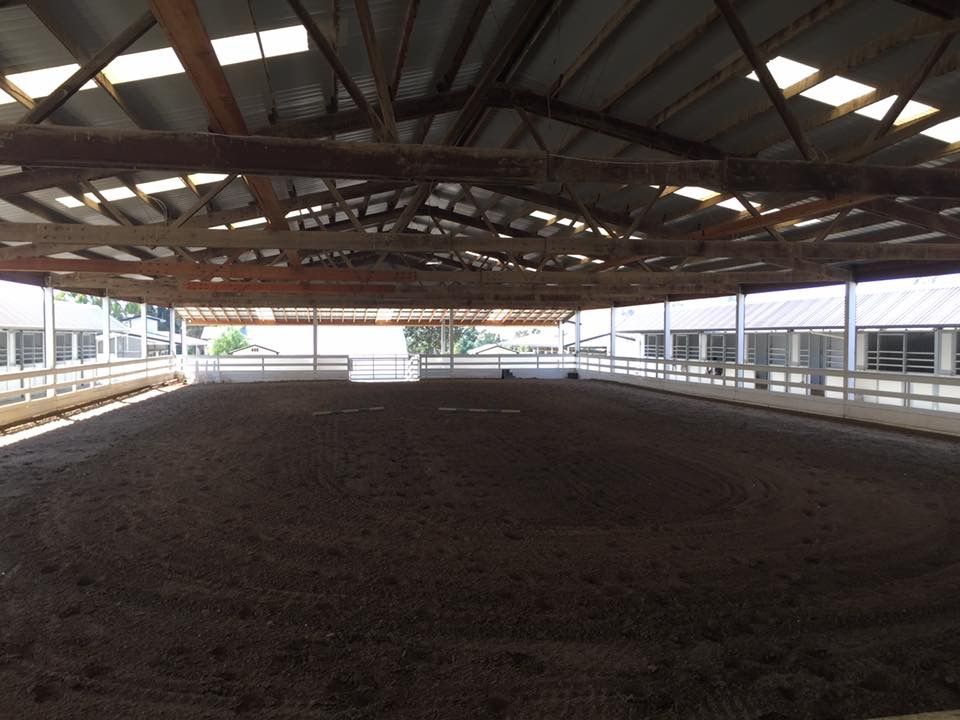 Covered horse arena with dirt floor and metal roof, viewed from one end