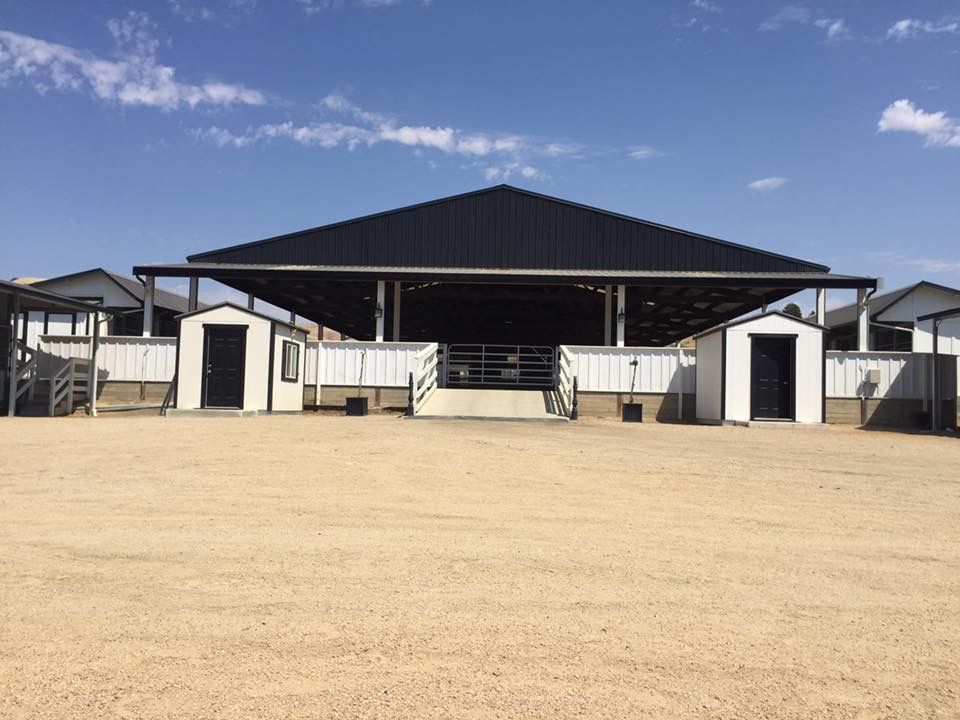 Outdoor equestrian arena with white stalls and a large black-roofed grandstand under a blue sky