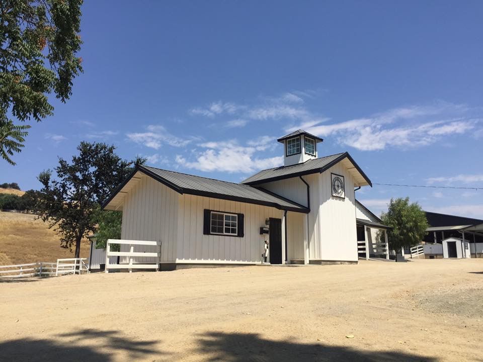 White barn-style building with a cupola on a sandy lot under a blue sky