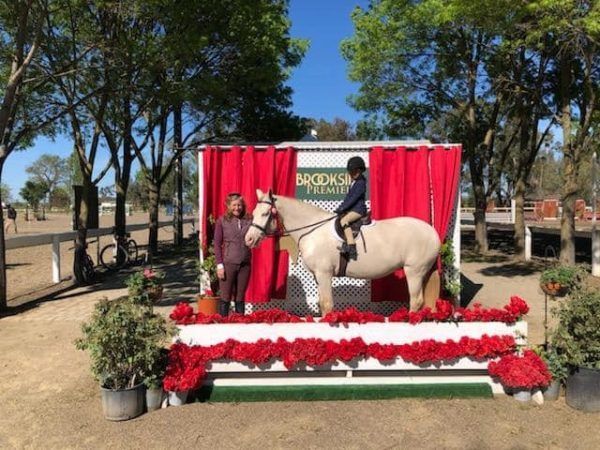 Woman with a horse on a red-draped stage, decorated with flowers and trees in the background