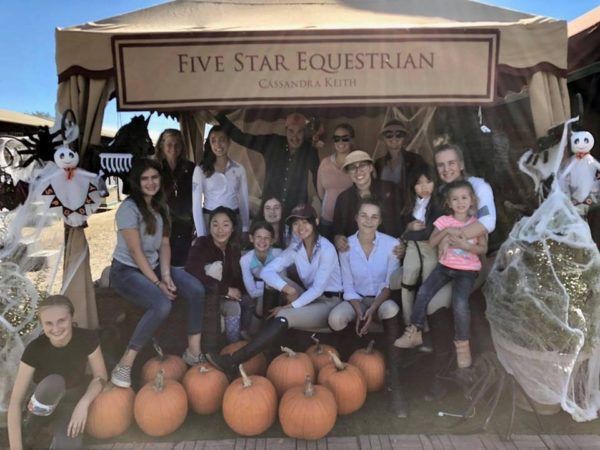 Group posing at a horse farm booth with pumpkins and Halloween decorations under a tent.