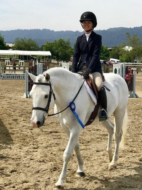 Rider on a white horse in an outdoor arena, with hills and fences in the background.