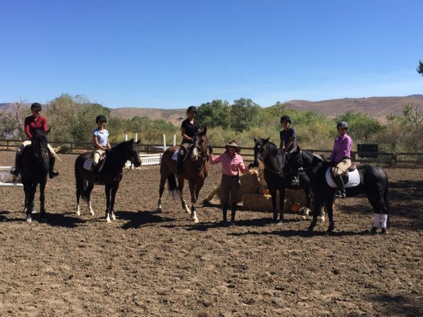 Group of horseback riders and a standing person in a dry field under a clear blue sky