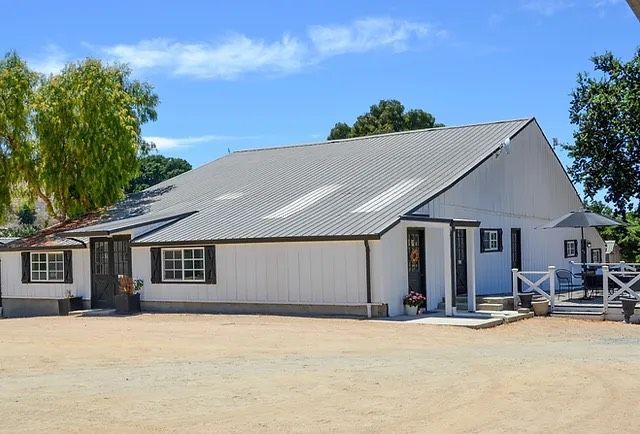 White barn-style building with gray roof and small porch under a blue sky