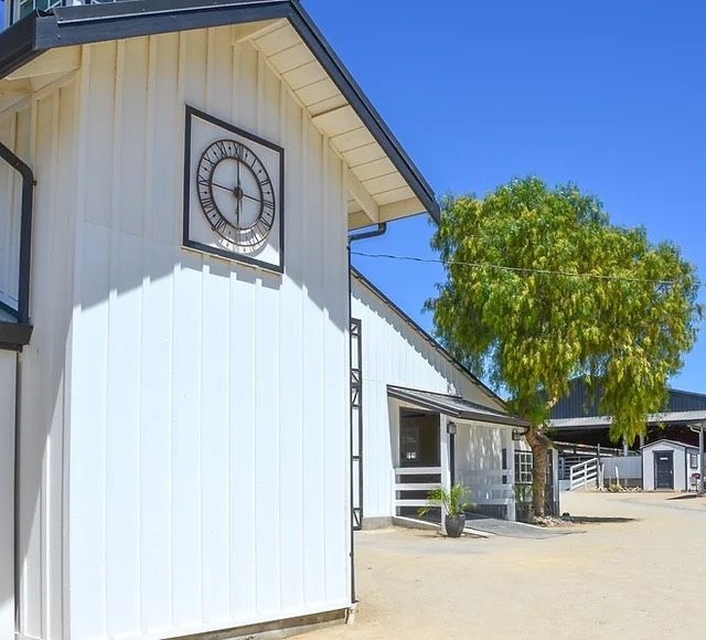 White building with a decorative clock under the eaves, beside a sunny courtyard and green tree
