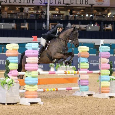 Horse and rider clearing a colorful show jumping obstacle at an indoor arena