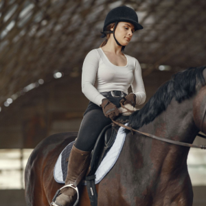 Rider in a black helmet on a dark horse inside an indoor riding arena