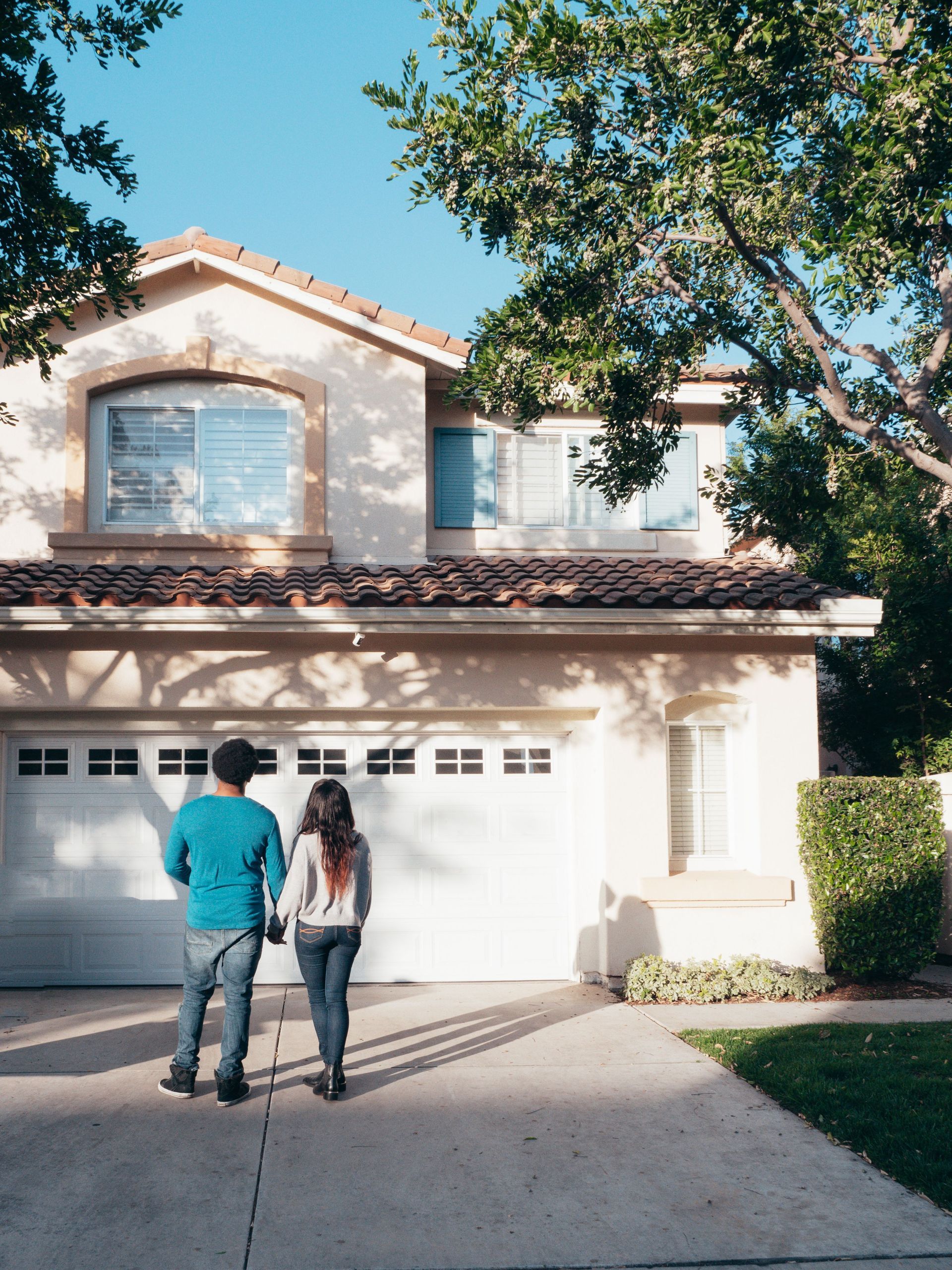 Two people standing in front of a suburban house and garage driveway