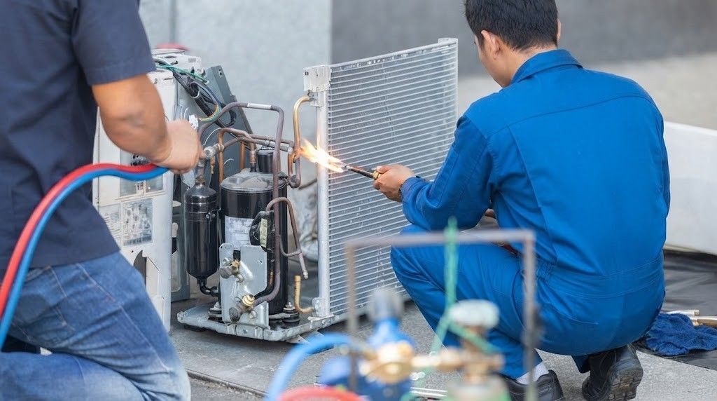 Technicians in blue work on industrial equipment with hoses and gauges in a workshop
