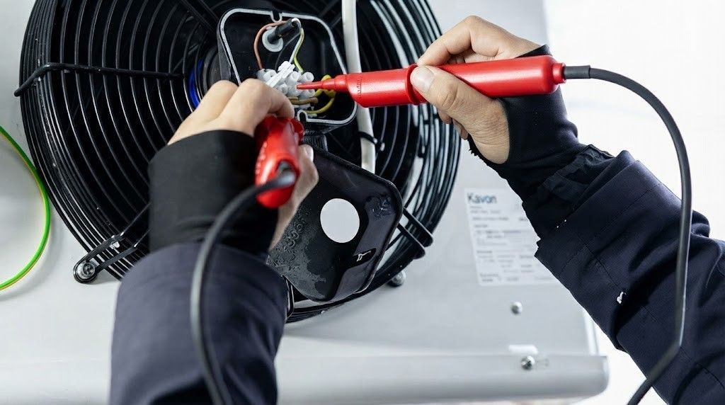 Hands using red tools to repair a black fan unit on an air conditioner outdoors