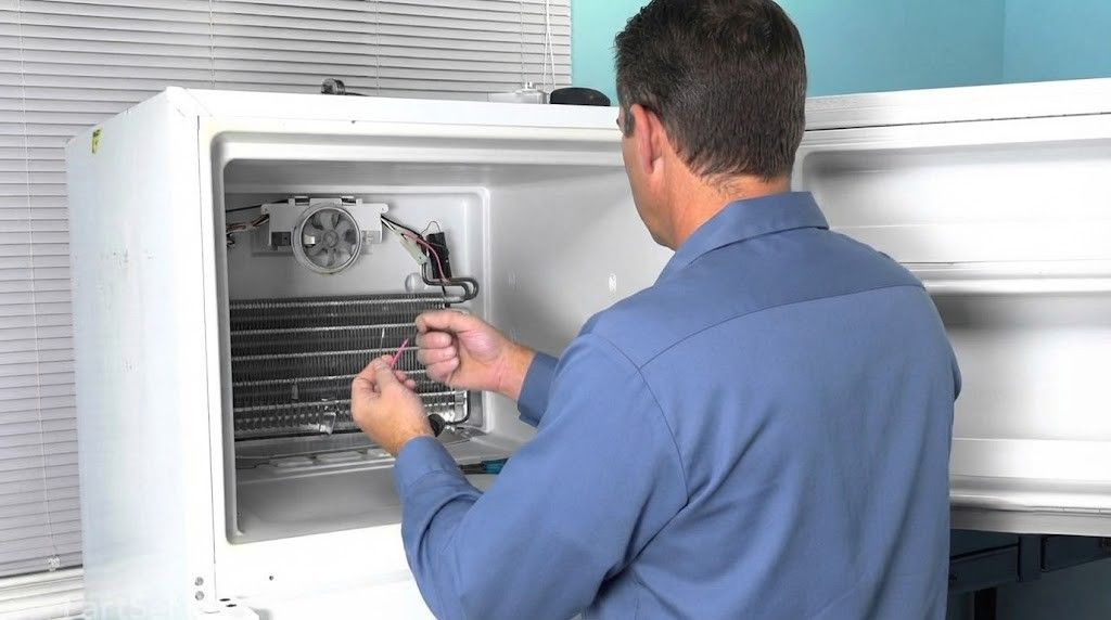 Technician inspecting the inside of a white industrial refrigerator or freezer with tools.