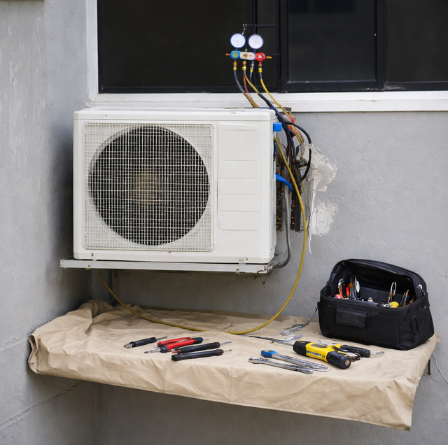 Outdoor air conditioner unit being serviced, with tools and gauges on a covered workbench.