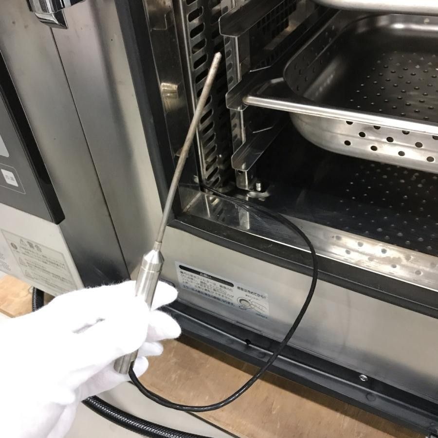 Gloved hand holding a cable near the open door of a stainless steel appliance with metal racks