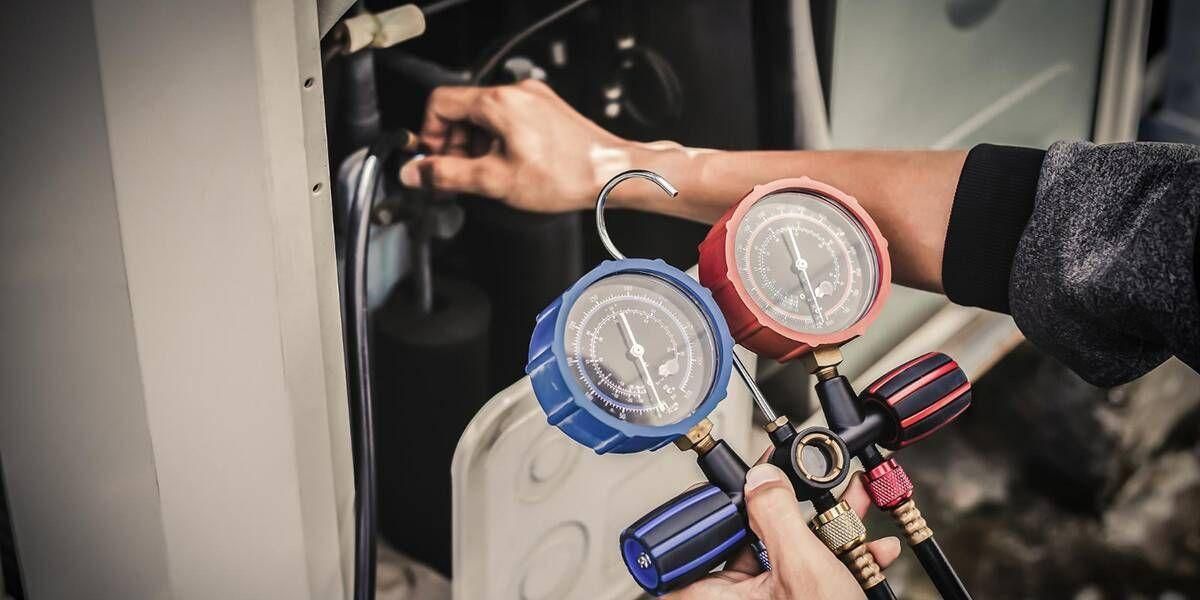Mechanic connecting dual gauges to an air conditioning service port in a car engine bay