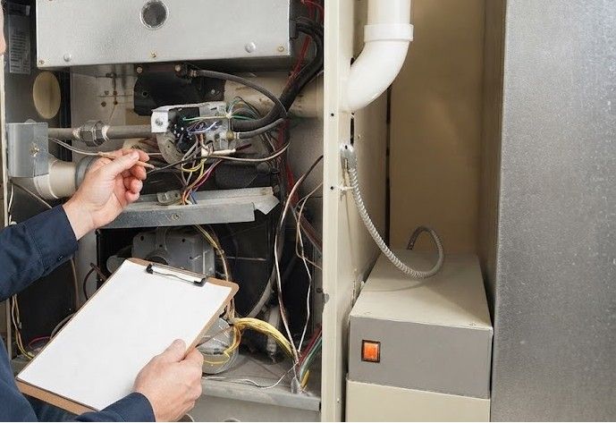 Technician inspecting furnace wiring with a clipboard in an equipment closet