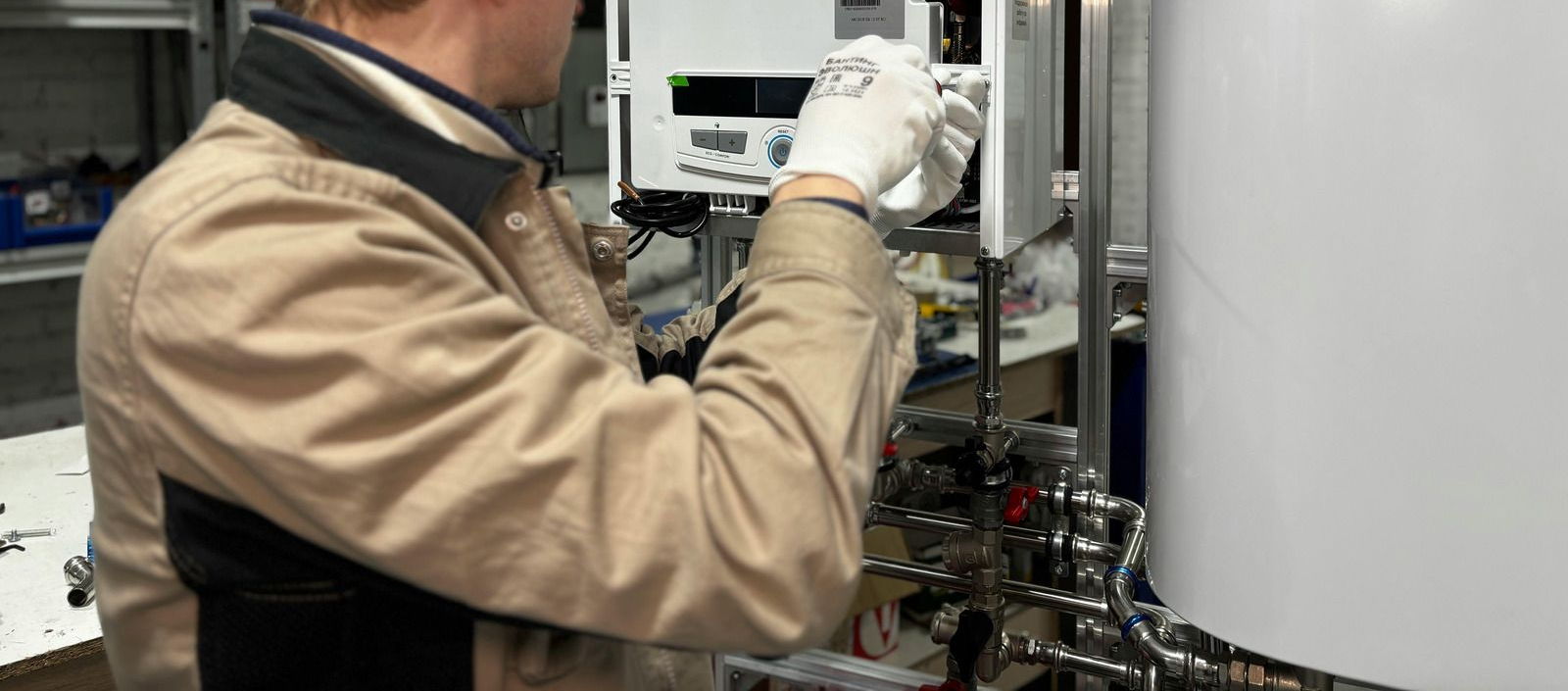 Technician in a tan jacket adjusts machinery with gloved hands in a lab or industrial setting