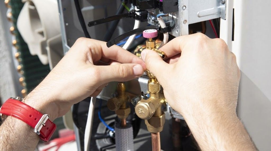 Hands adjusting brass plumbing valves and wires inside an HVAC unit