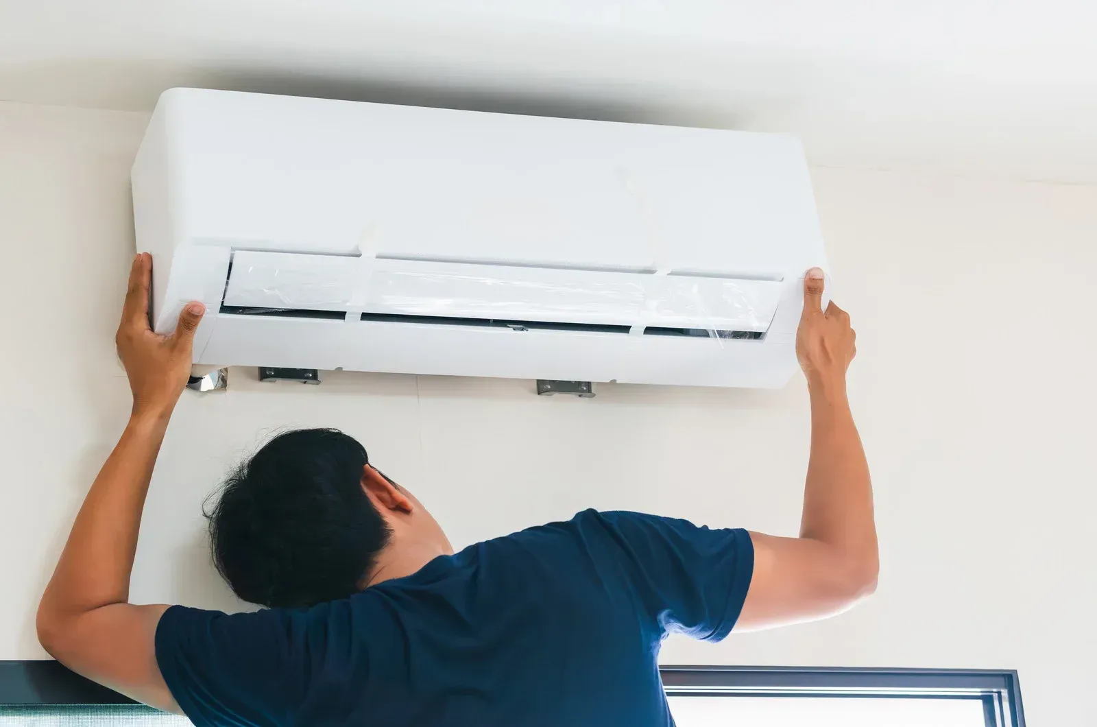 Person installing a white wall-mounted air conditioner indoors