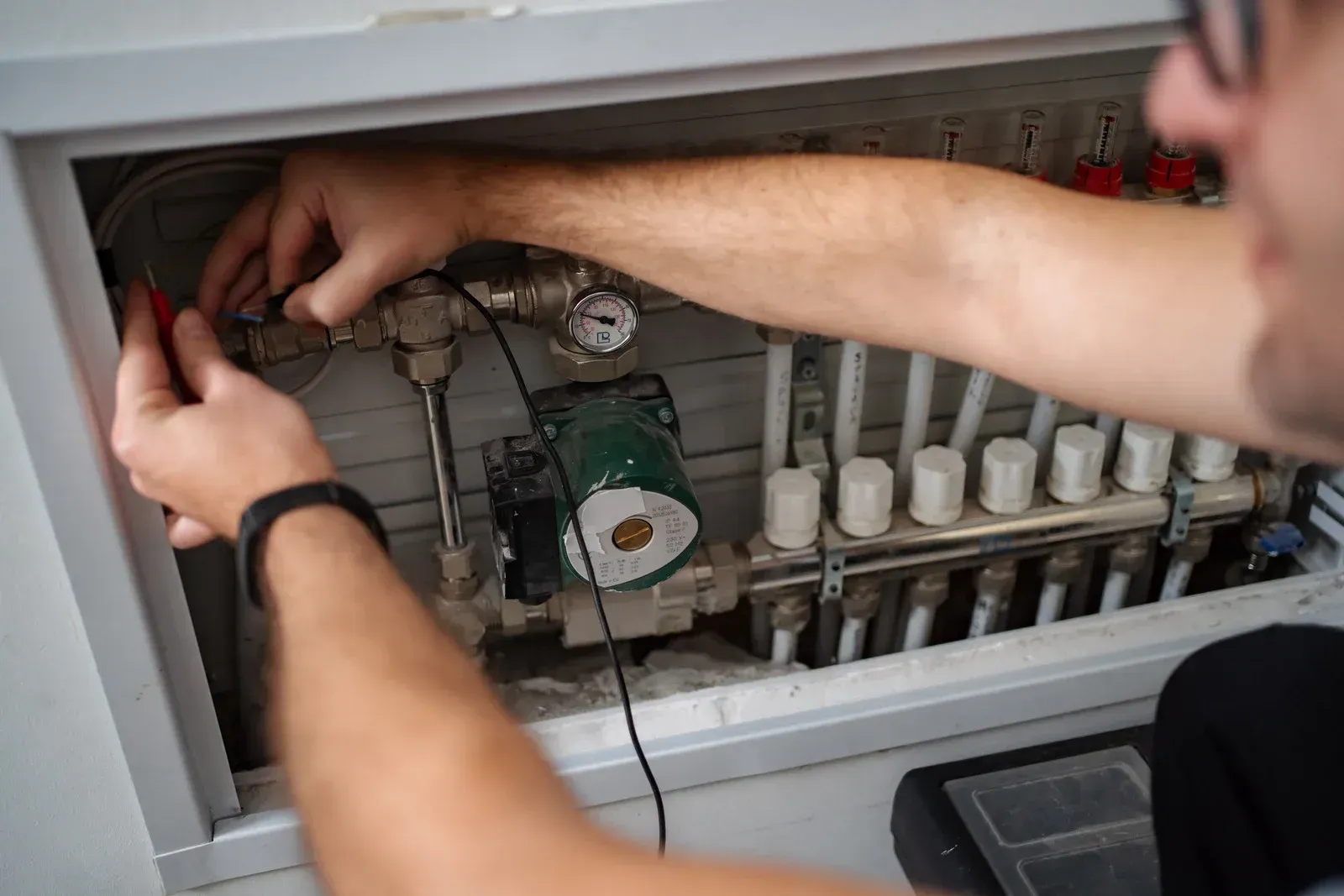Person repairing wiring inside an electrical panel with fuses and pipes.