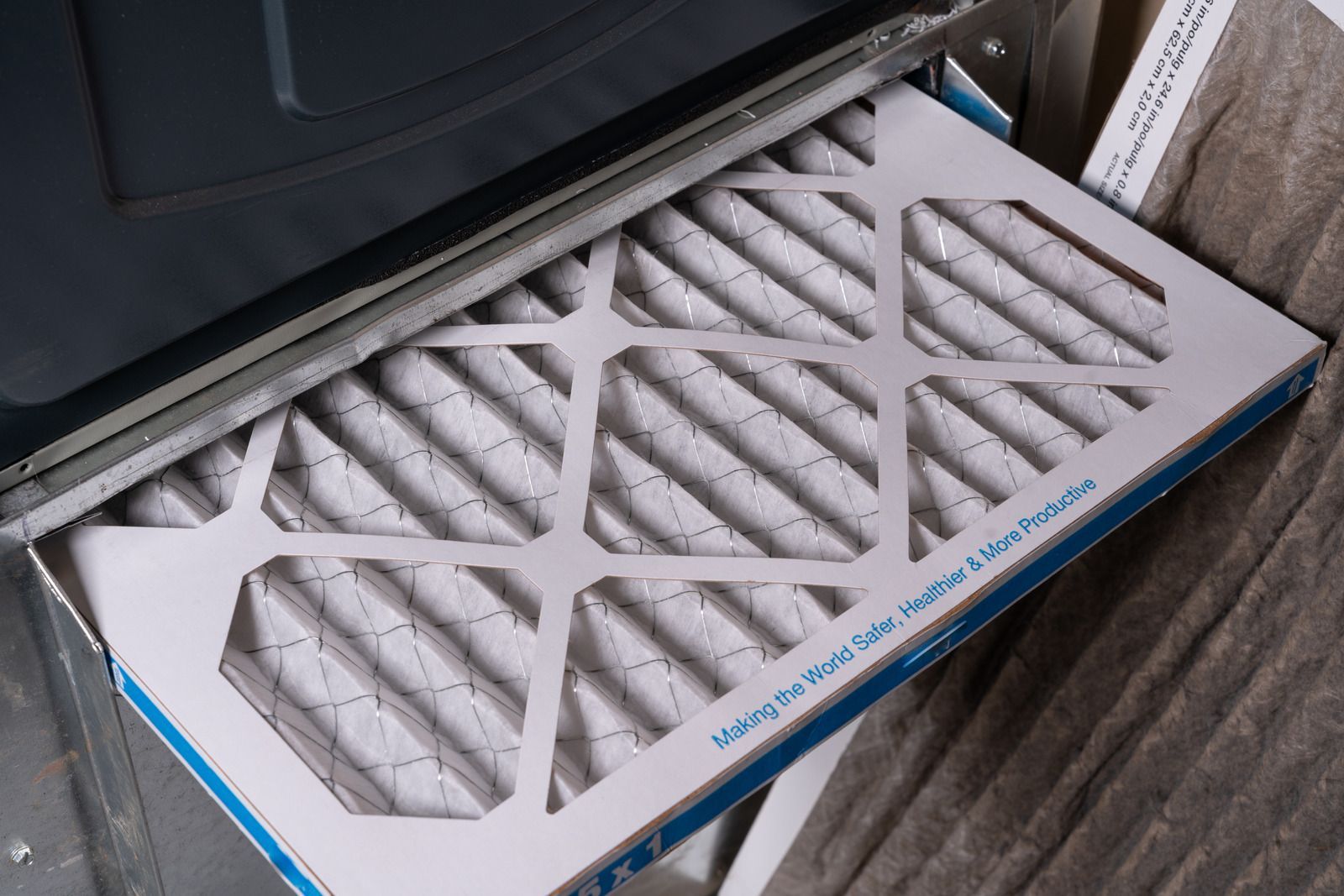 Air conditioner filter panel with white mesh leaning against a dark appliance on a wooden floor