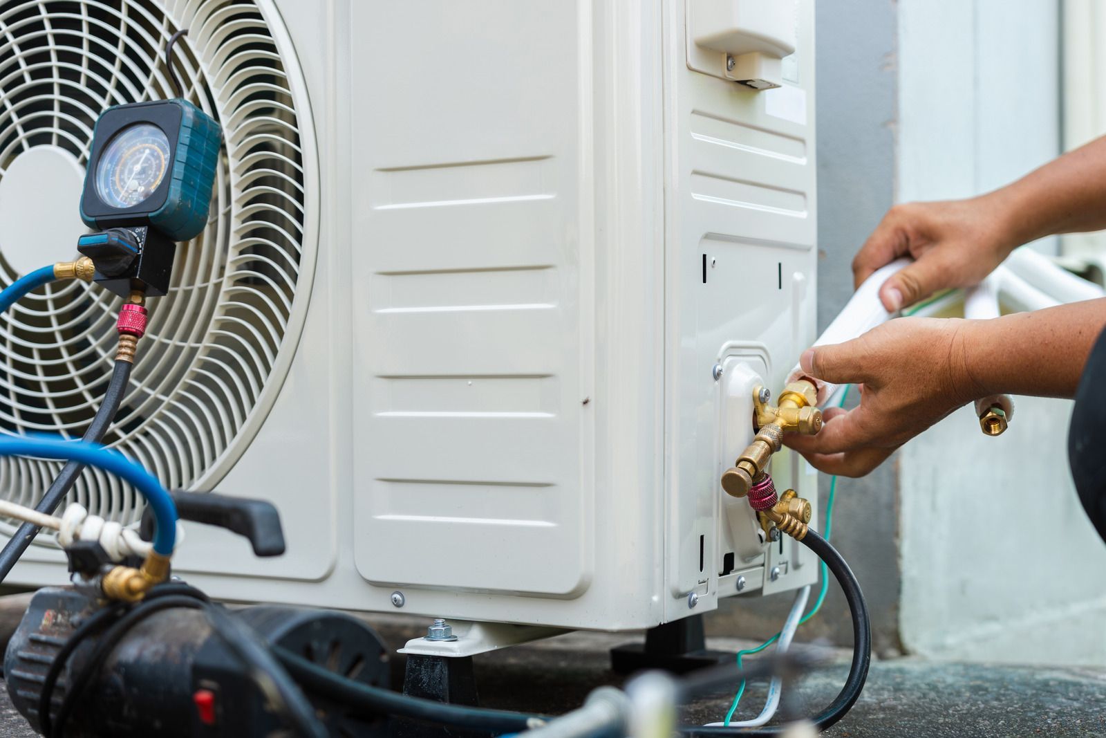 Technician connecting gauges to an outdoor air conditioner unit for maintenance