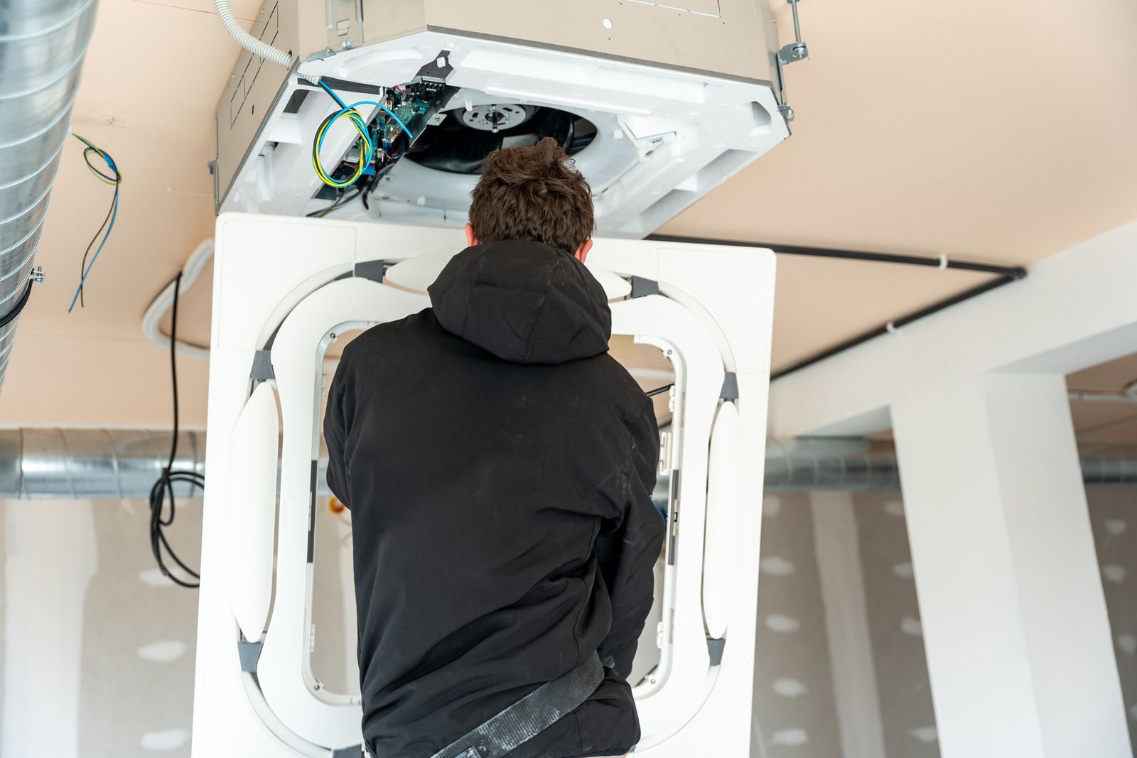 Technician working inside an open ceiling-mounted machine in a bright room