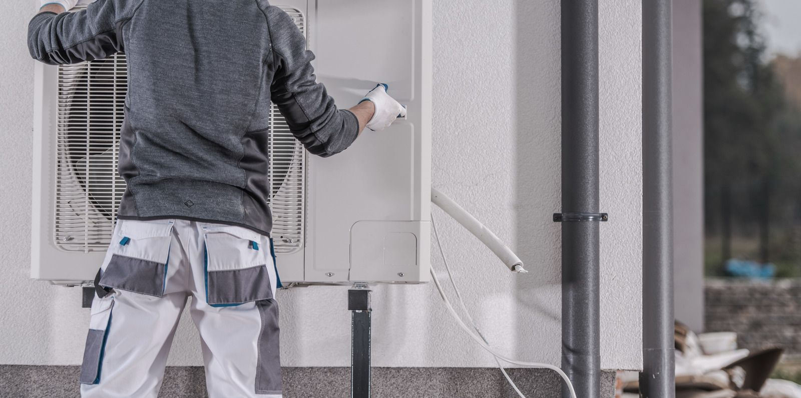 Worker cleaning an outdoor air-conditioning unit beside a building wall