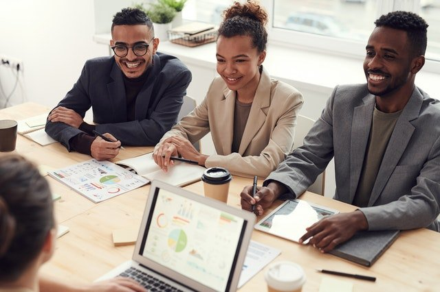 A group of people are sitting around a table with a laptop.