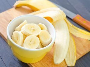 A bowl of sliced bananas next to a peeled banana on a cutting board.