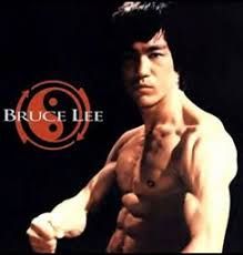 Bruce lee without a shirt is standing in front of a black background.